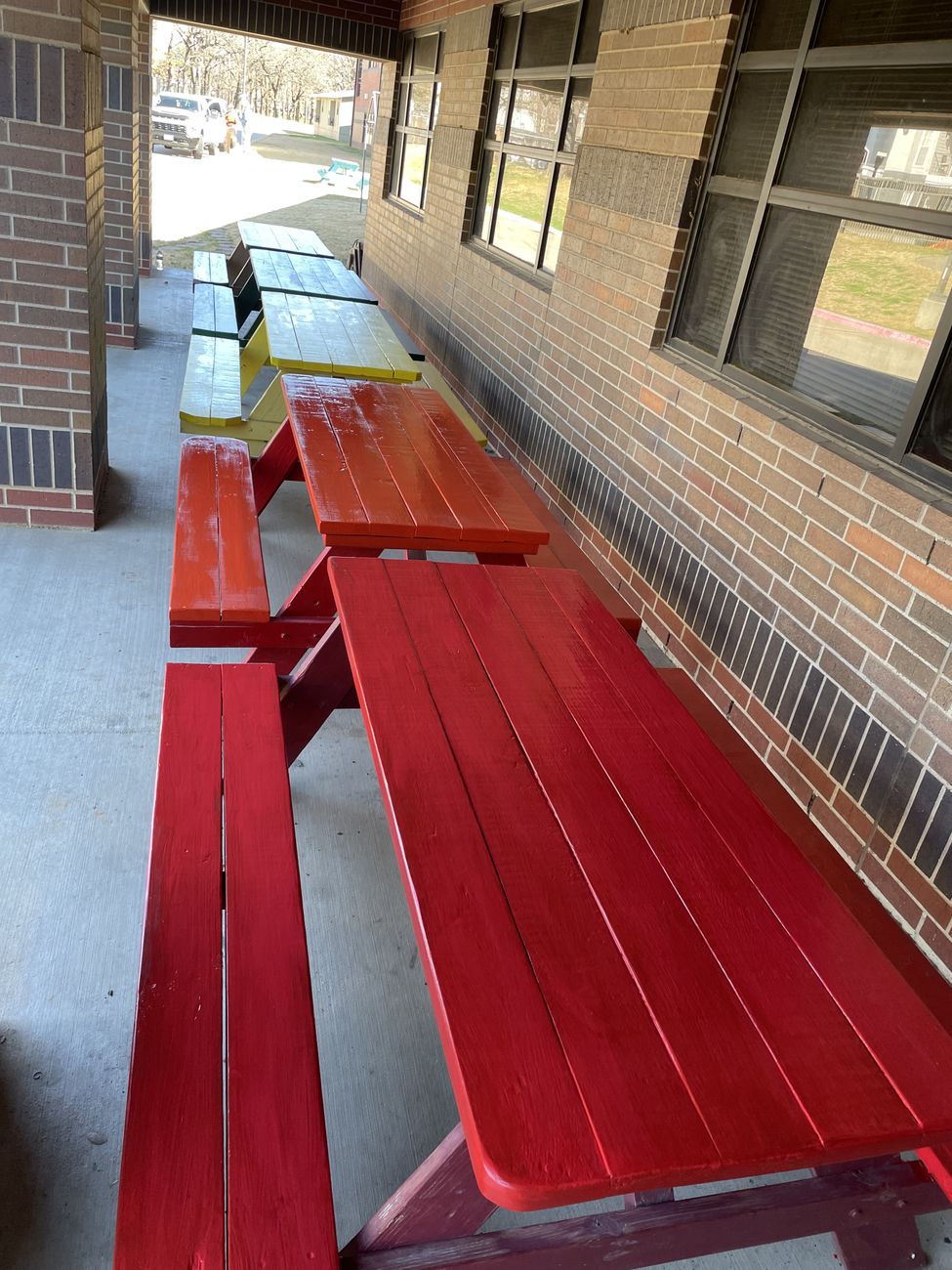 Freshly painted red and yellow picnic tables outside a school