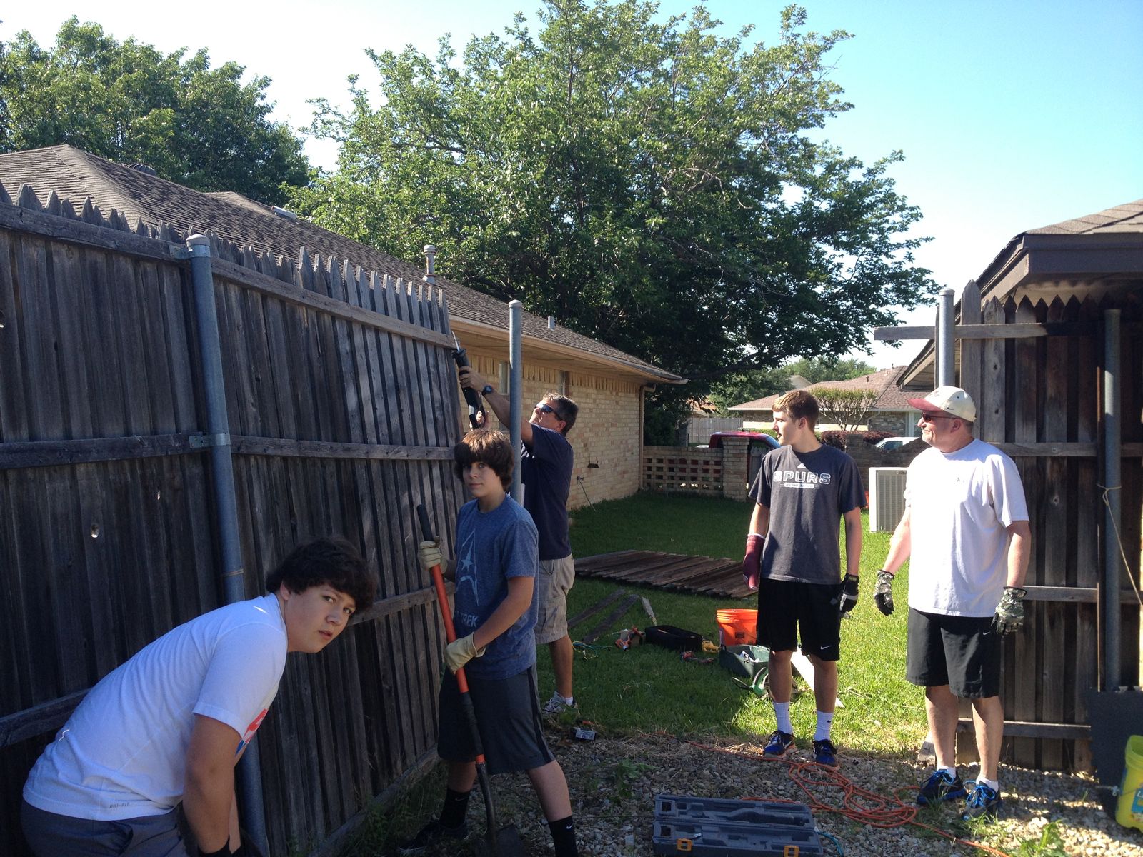 Volunteers repairing a wooden backyard fence with tools and ladders